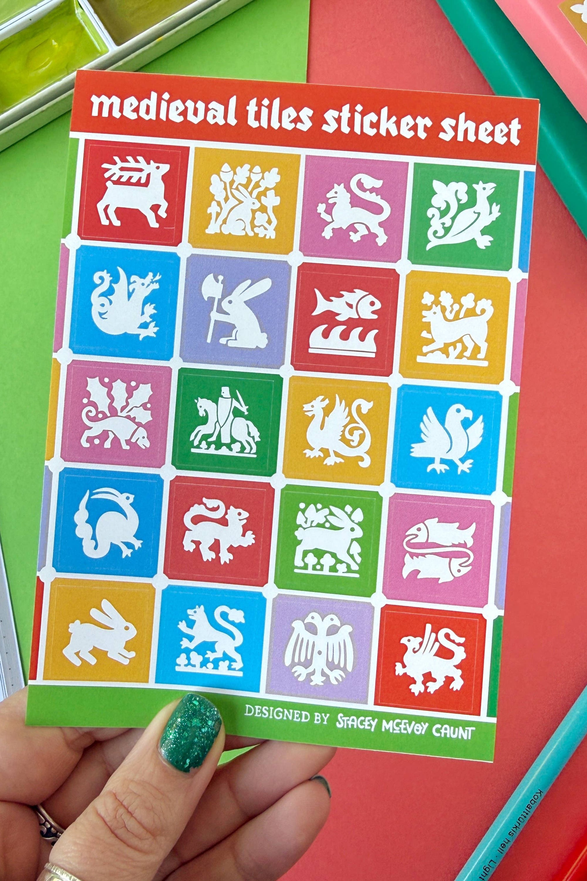 Sheet of medieval tiles stickers held by a hand with colorful stationery items in the background.