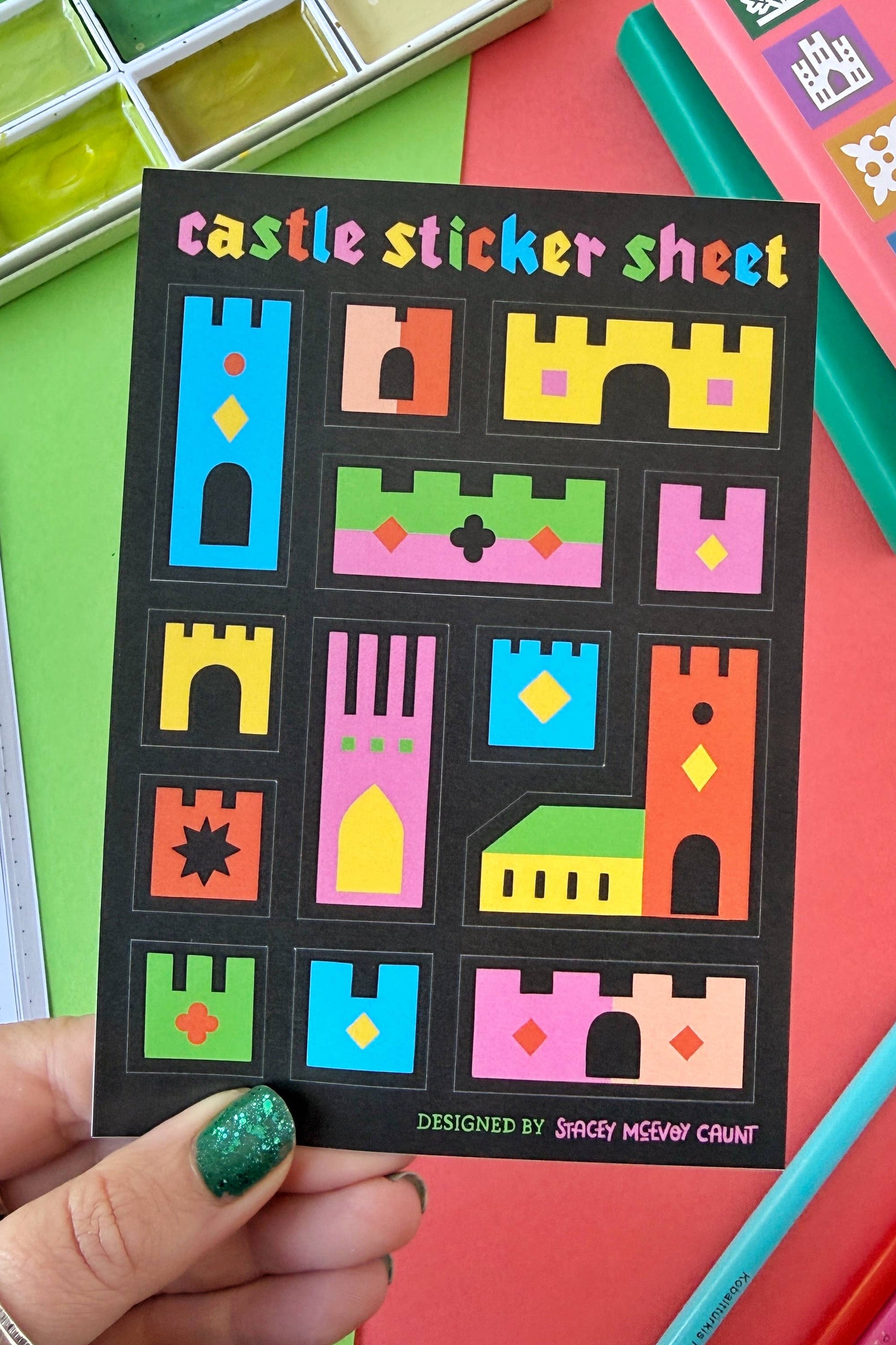 Castle sticker sheet held by a hand with colorful stationery items on a multicolored background