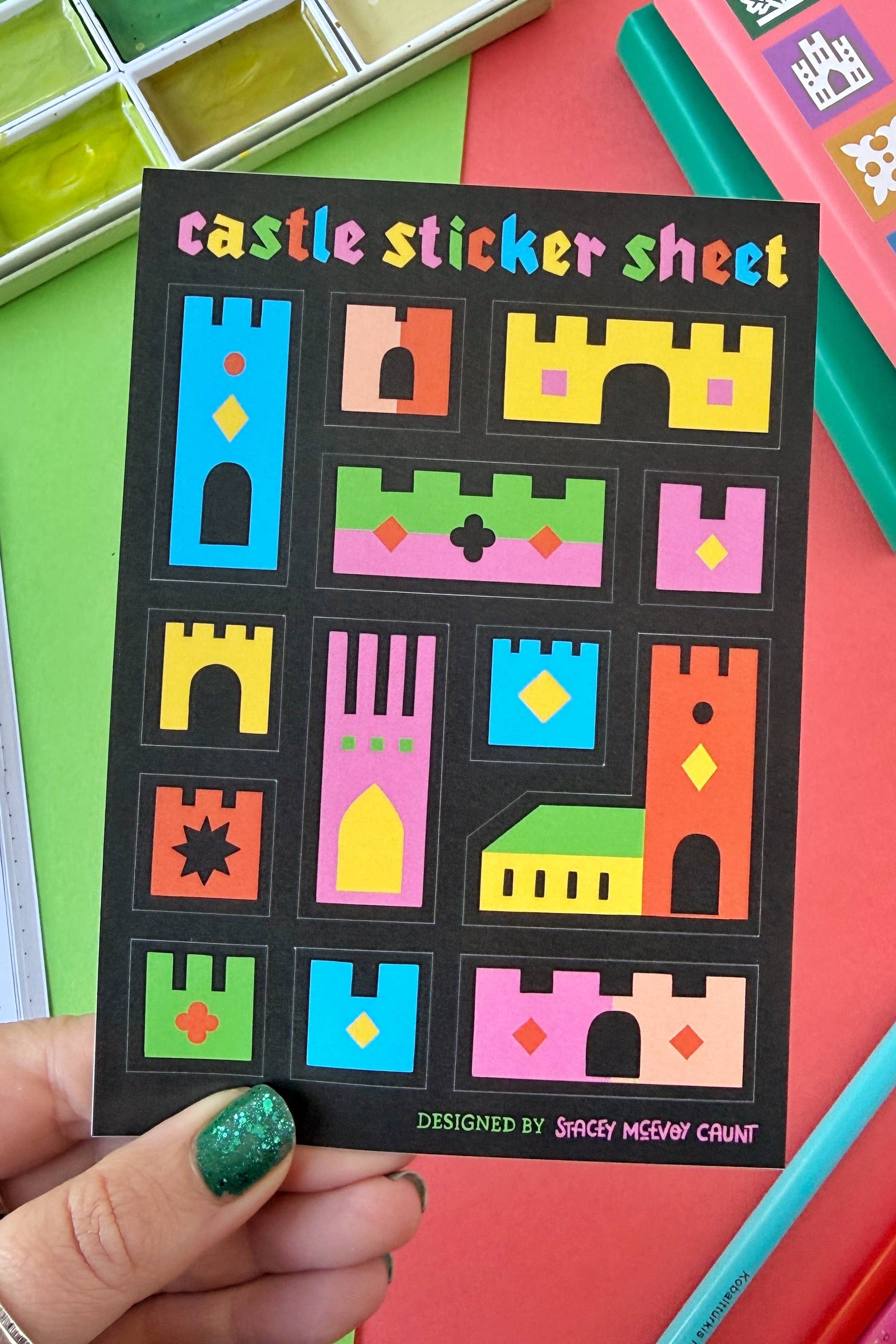 Castle sticker sheet held by a hand with colorful stationery items on a multicolored background