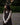 Woman in a brown dress layerd over an off-white long sleeve t-shirt featuring fruit patterns standing outdoors.