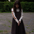 Woman wearing a brown dress layered over a cream long sleeved t-shirt featuring orange patterns outdoors.