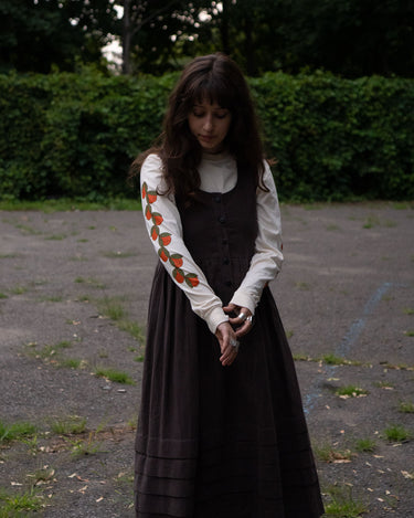 Woman wearing a brown dress layered over a cream long sleeved t-shirt featuring orange patterns outdoors.
