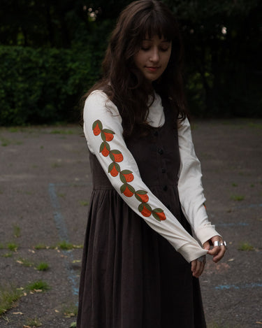Woman wearing an off-white long-sleeve shirt with orange designs, standing outdoors.