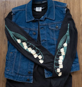 Black long-sleeved tee with lily of the valley flowers prited down the sleeves layered under a denim vest