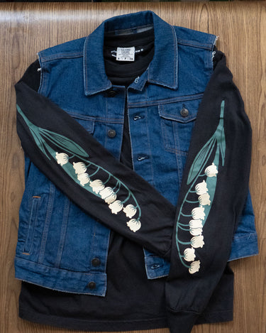 Black long-sleeved tee with lily of the valley flowers prited down the sleeves layered under a denim vest