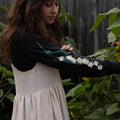 Woman wearing a black long-sleeved tee with white floral patterns in a garden setting