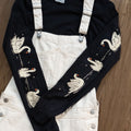 Black long-sleeved t-shirt with swans printed down each arm layered under off-white overalls.