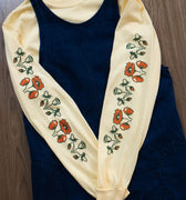 Butter yellow long-sleeved t-shirt with orangey red and green poppy floral pattern layered under a denim pinafore dress