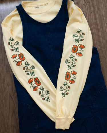 Butter yellow long-sleeved t-shirt with orangey red and green poppy floral pattern layered under a denim pinafore dress