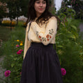 Woman wearing a long-sleeved shirt with floral print sleeves and dark skirt standing in a garden.