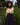 Woman wearing a long-sleeved shirt with floral print sleeves and dark skirt standing in a garden.