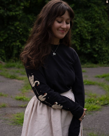 Woman wearing a black long-sleeved t-shirt with swans printed down the sleeves