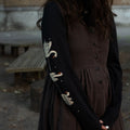 Woman wearing a brown dress and black long-sleeved tee with white swan print outdoors.