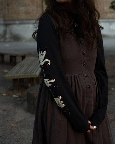 Woman wearing a brown dress and black long-sleeved tee with white swan print outdoors.