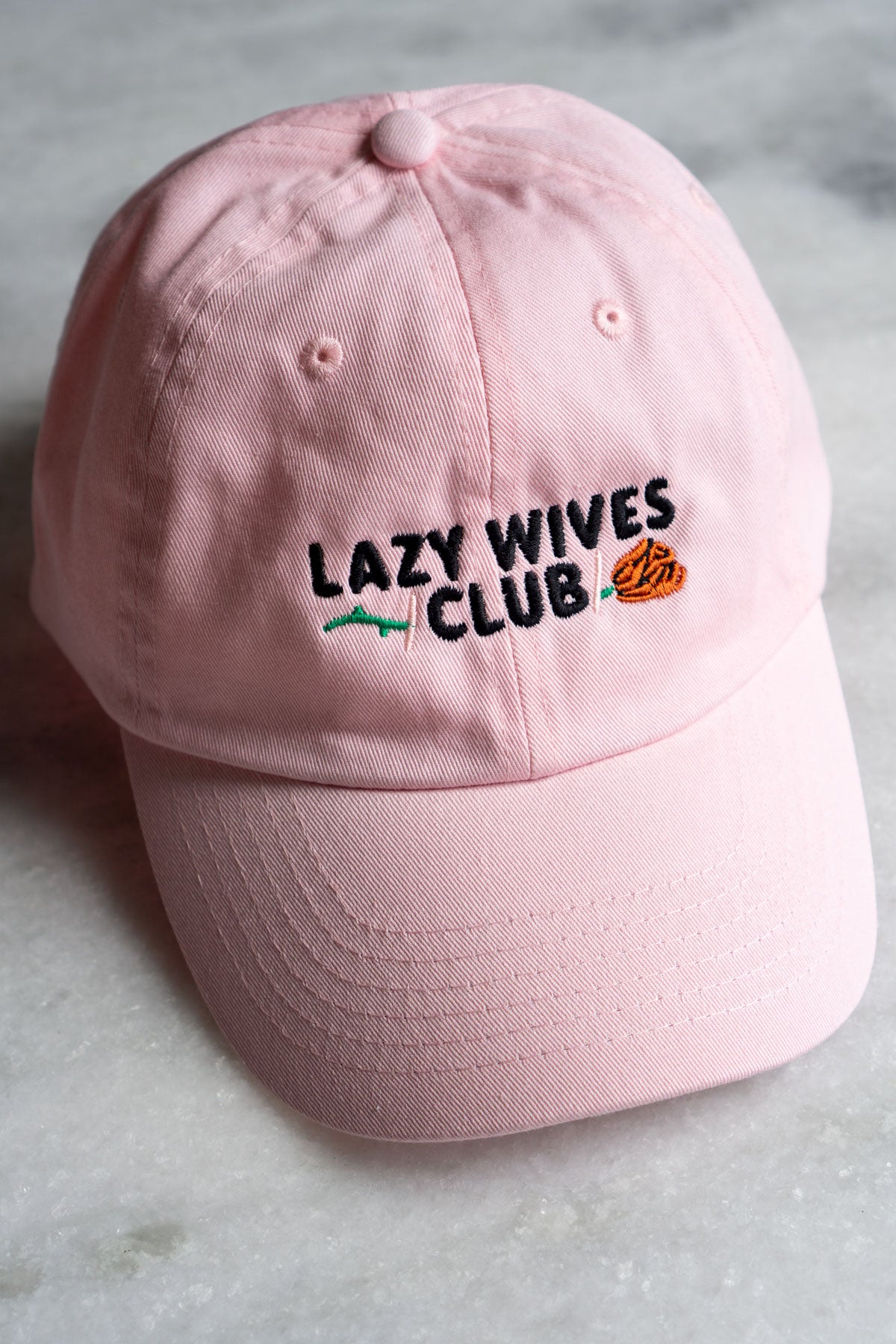 pale pink baseball cap with black embriodery text saying lazy wives club with red rose with green stem behind text