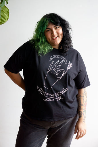 Model wearing loose fitting black t-shirt with illustrated print of a hand lighting a match and readin "set fire to everyone who has hurt you"