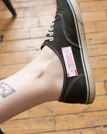 A sneaker adorned with a patch in the style of a fortune cookie insert, with text reading "bask in the glory of being alone"