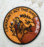 Round embroidered patch in tones of yellow and brown with imagery of a crying eagle and the words "I Shouldn't Act This Way in Public"
