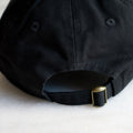 closeup of the back of black baseball hat with brass clasp 