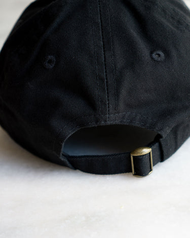 closeup of the back of black baseball hat with brass clasp 