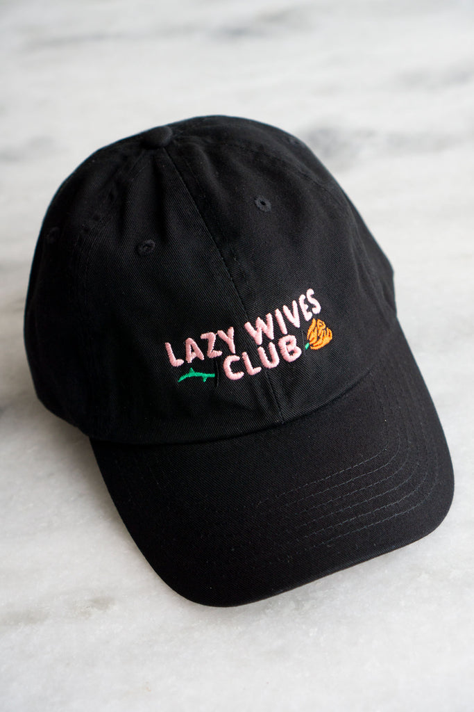 black baseball cap with pale pink embroidery text saying lazy wives club with red rose with green stem behind text